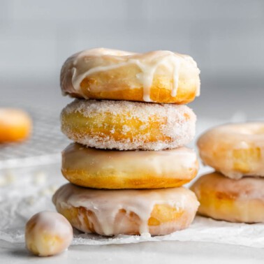 A stack of glazed donuts on a kitchen counter, with donut holes nearby.