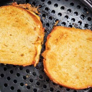 Overhead view inside an air fryer basket with two grilled cheese sandwiches.