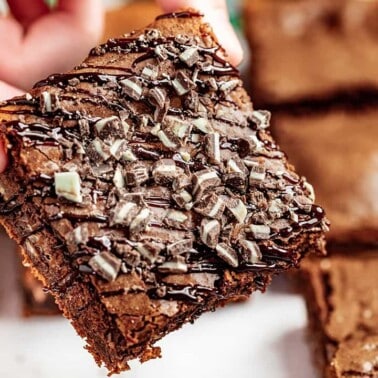 Close up view of someone's hand holding a brownie with Andes mints crushed on top.