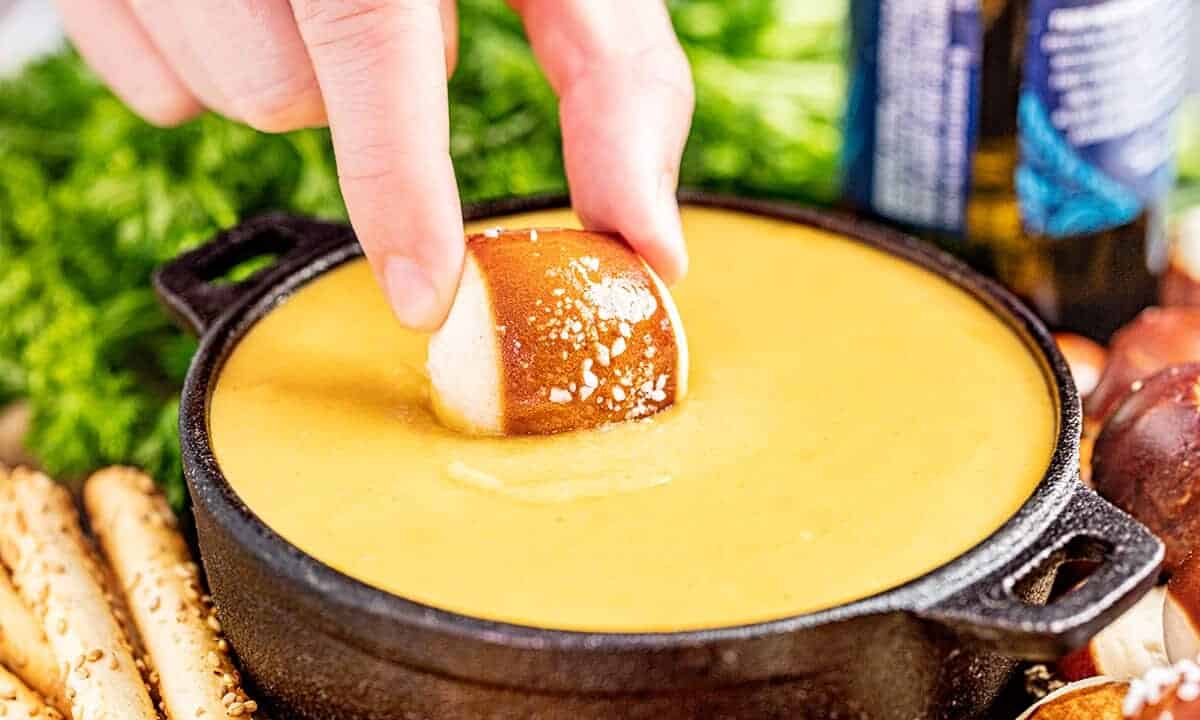 A hand dipping a pretzel bite into beer cheese dip.