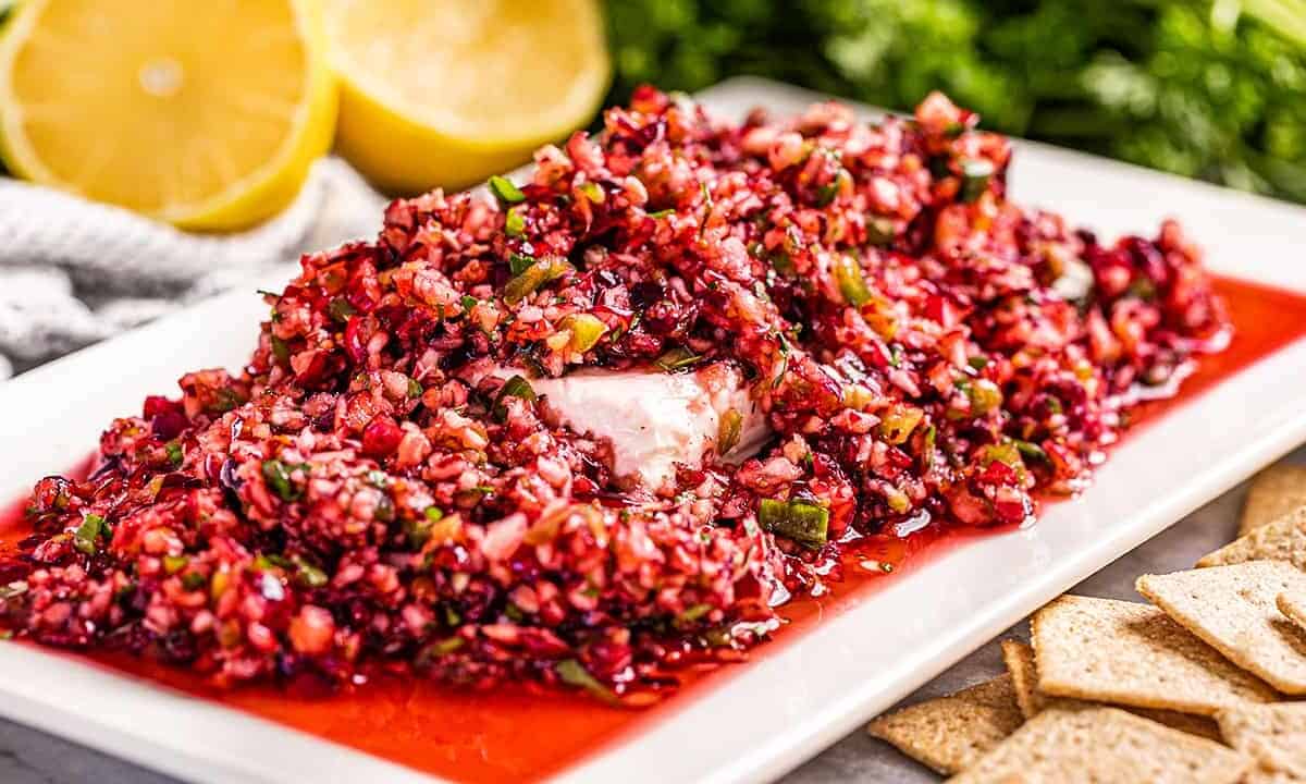 A serving plate full of cranberry salsa on top of a block of cream cheese.