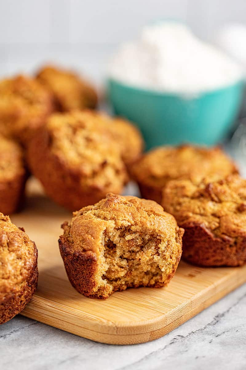 Freshly baked bran muffins on a cutting board. One has a bite taken out of it.