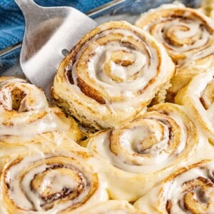 A spatula picking up a cinnamon roll from the glass baking dish.