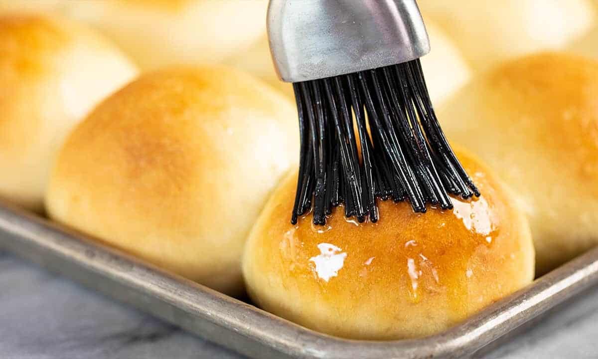 Roll being brushed with butter on a baking sheet.