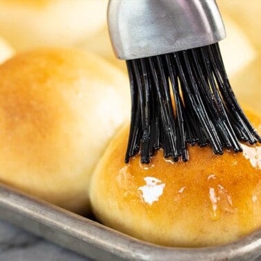 Roll being brushed with butter on a baking sheet.