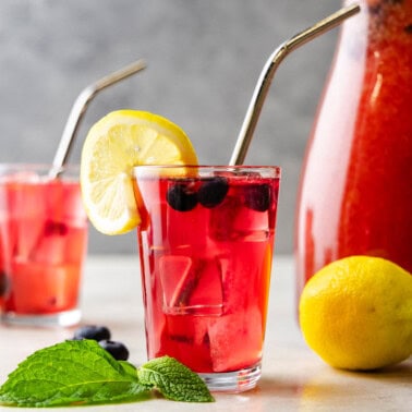 Two glasses of strawberry lemonade with a pitcher in the background.