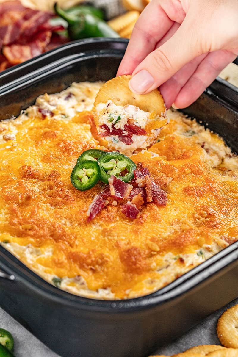 dipping a ritz cracker into cheesy jalapeno popper dip.