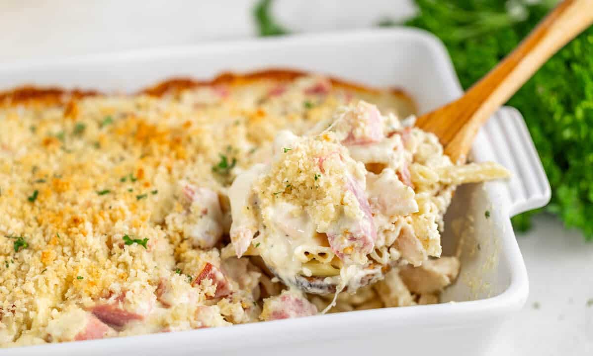 A wooden spoon dipped into a chicken cordon bleu casserole.