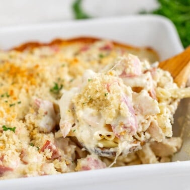 A wooden spoon dipped into a chicken cordon bleu casserole.