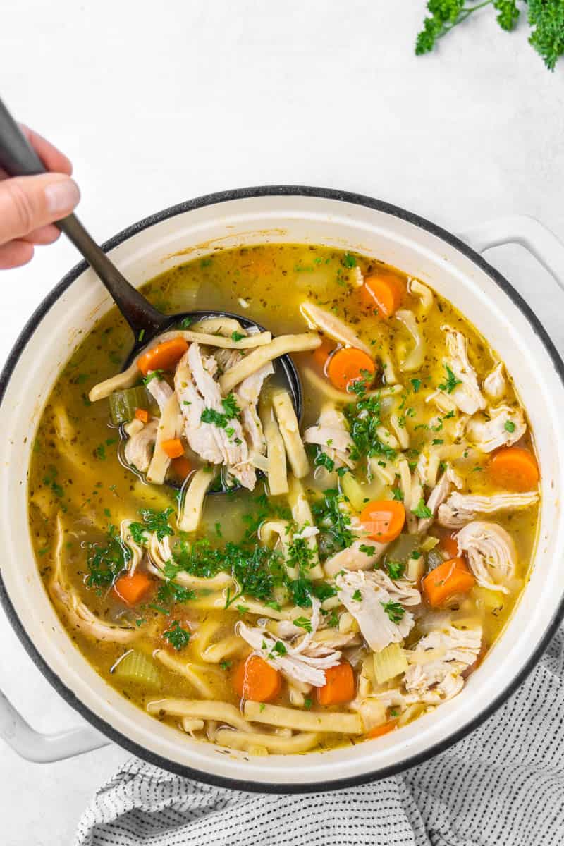 Overhead view of a pot filled with chicken noodle soup with a ladle resting in it.