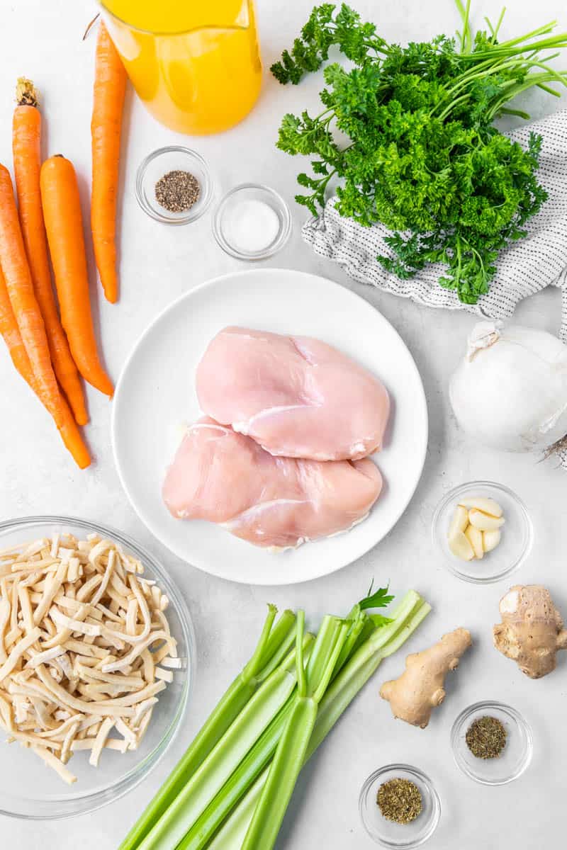 Overhead view of the raw ingredients needed to make chicken noodle soup on a clean kitchen counter.