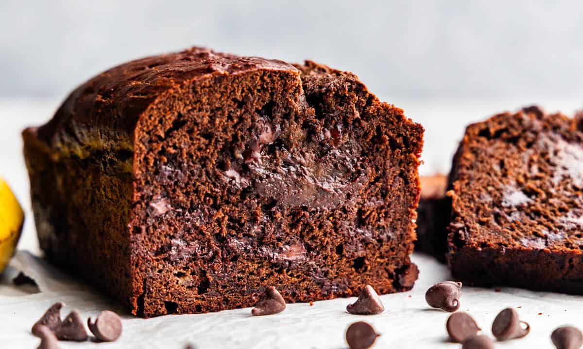 A loaf of chocolate banana bread cut with slices cut off, showing off the chocolate chips inside.