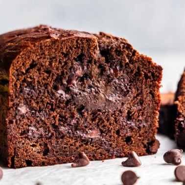 A loaf of chocolate banana bread cut with slices cut off, showing off the chocolate chips inside.