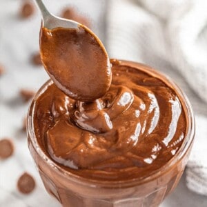 Bird's eye view of a spoon drizzling Chocolate Pudding in a glass dish full of chocolate pudding.