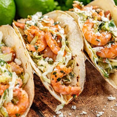 Three cilantro lime shrimp tacos on a wooden serving platter.