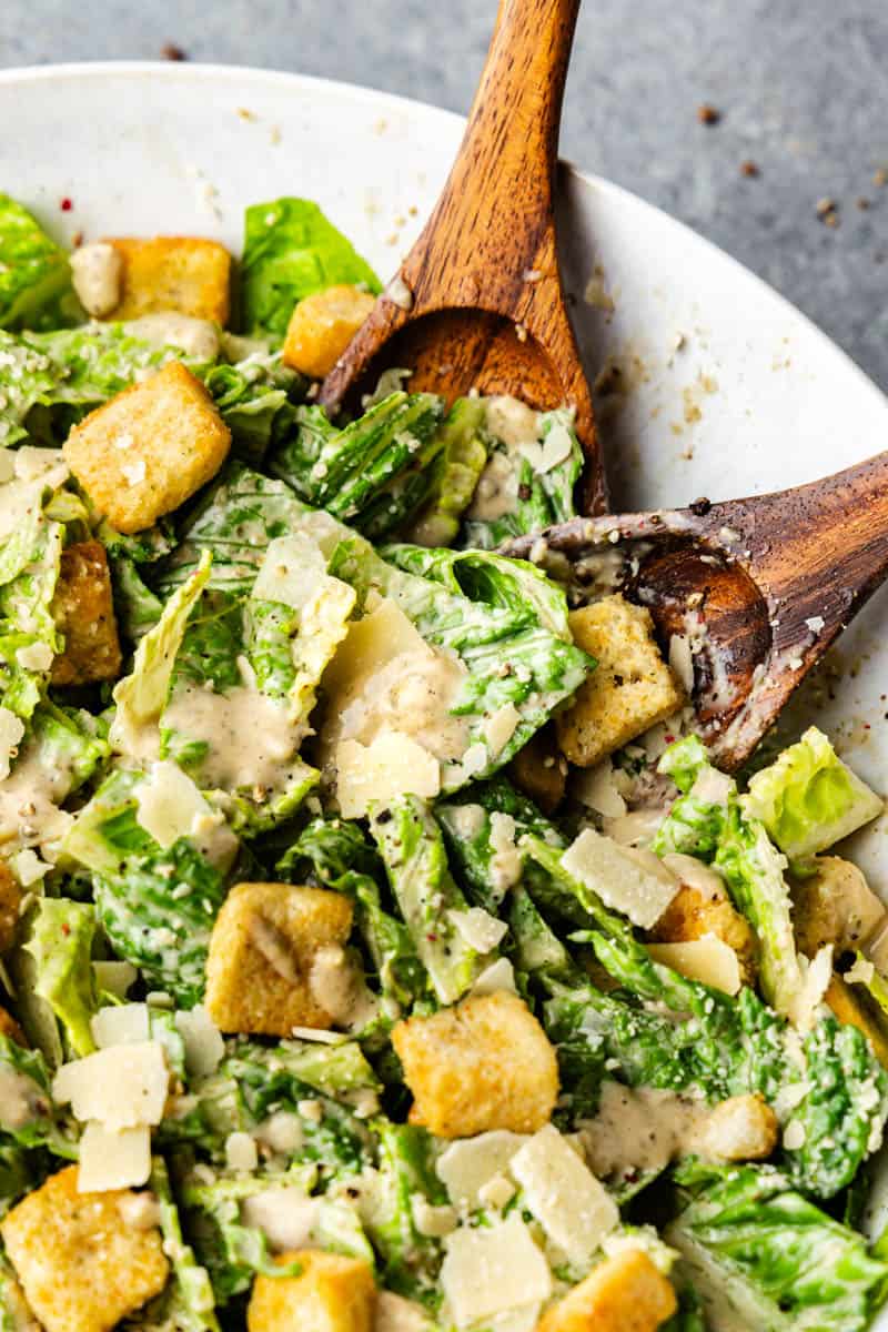 A bowl of classic Caesar Salad with two wooden spoons.