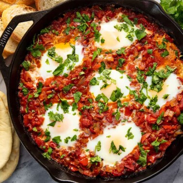 Bird's eye view of Shakshuka in a cast iron skillet surrounded by pita bread.