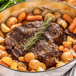 Pot roast surrounded by potatoes and carrots in a large pot.