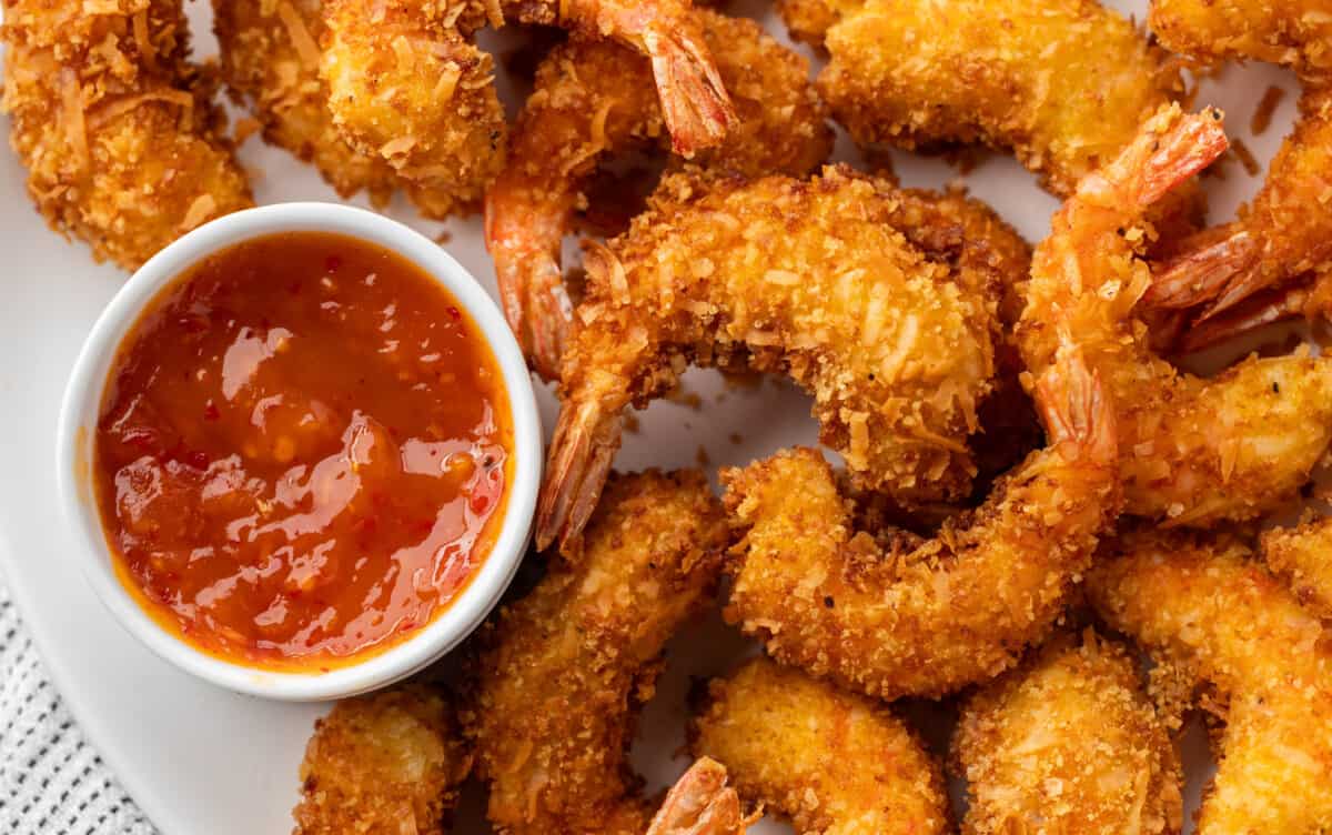 Overhead view of crispy coconut shrimp with dipping sauce on a serving platter.