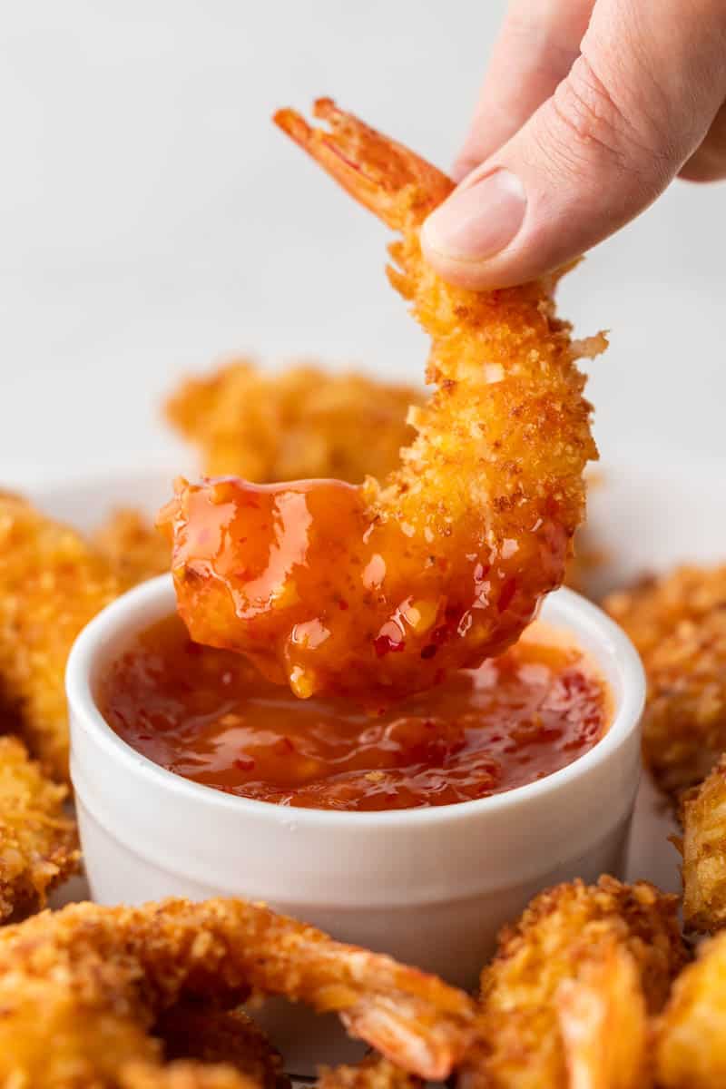 A hand dipping a crispy coconut shrimp into sauce.