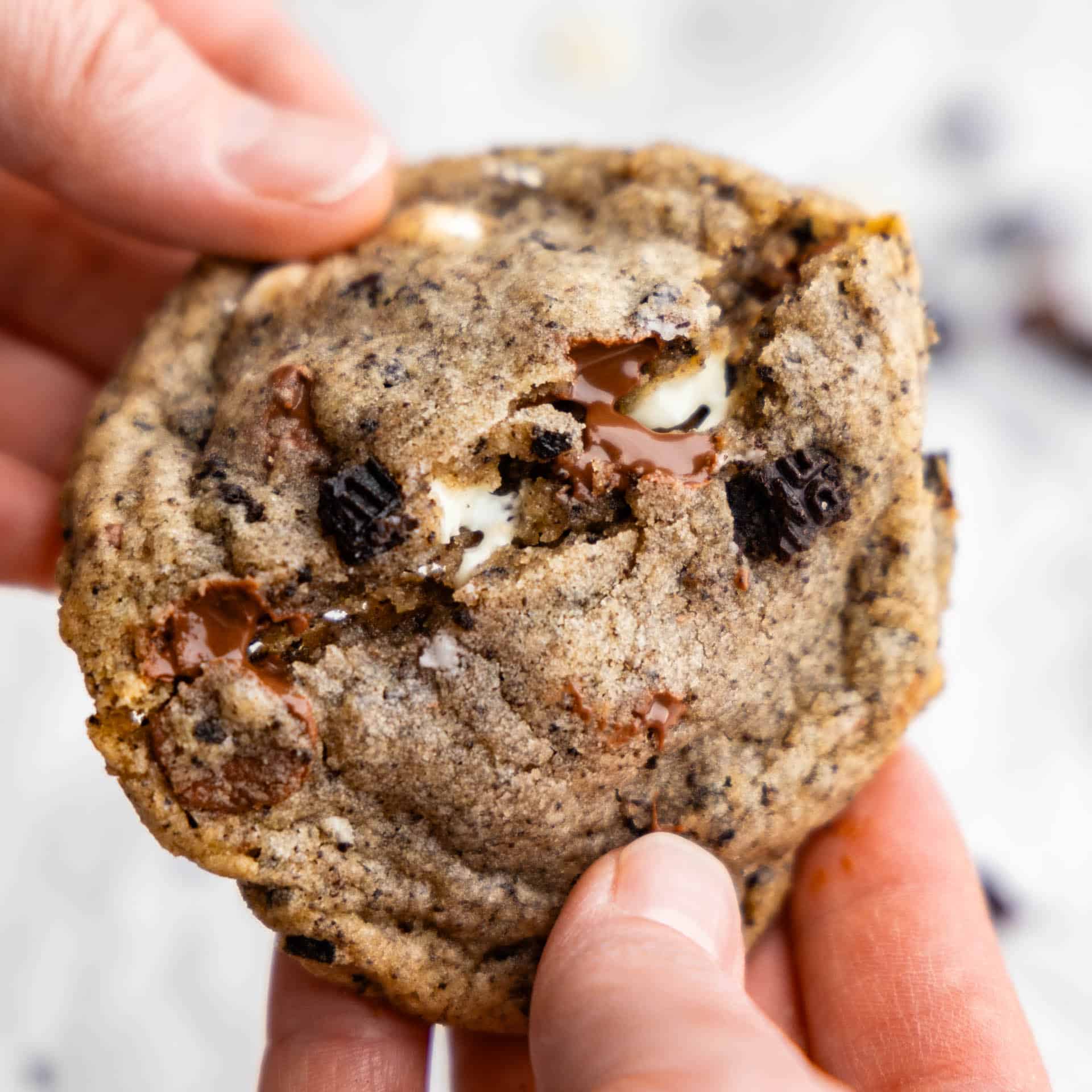 A close up view of a cookies and cream cookie being broken in half.