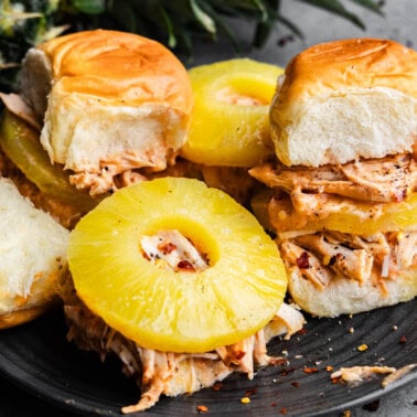 Cream cheese chicken sliders on a black plate. Some of them are open-faced to see the sliced pineapple in each slider.