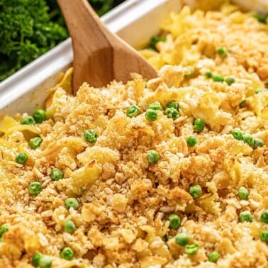 Creamy chicken casserole in white baking dish with wooden spoon.