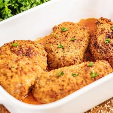 Crispy breaded pork chops in a white baking dish.