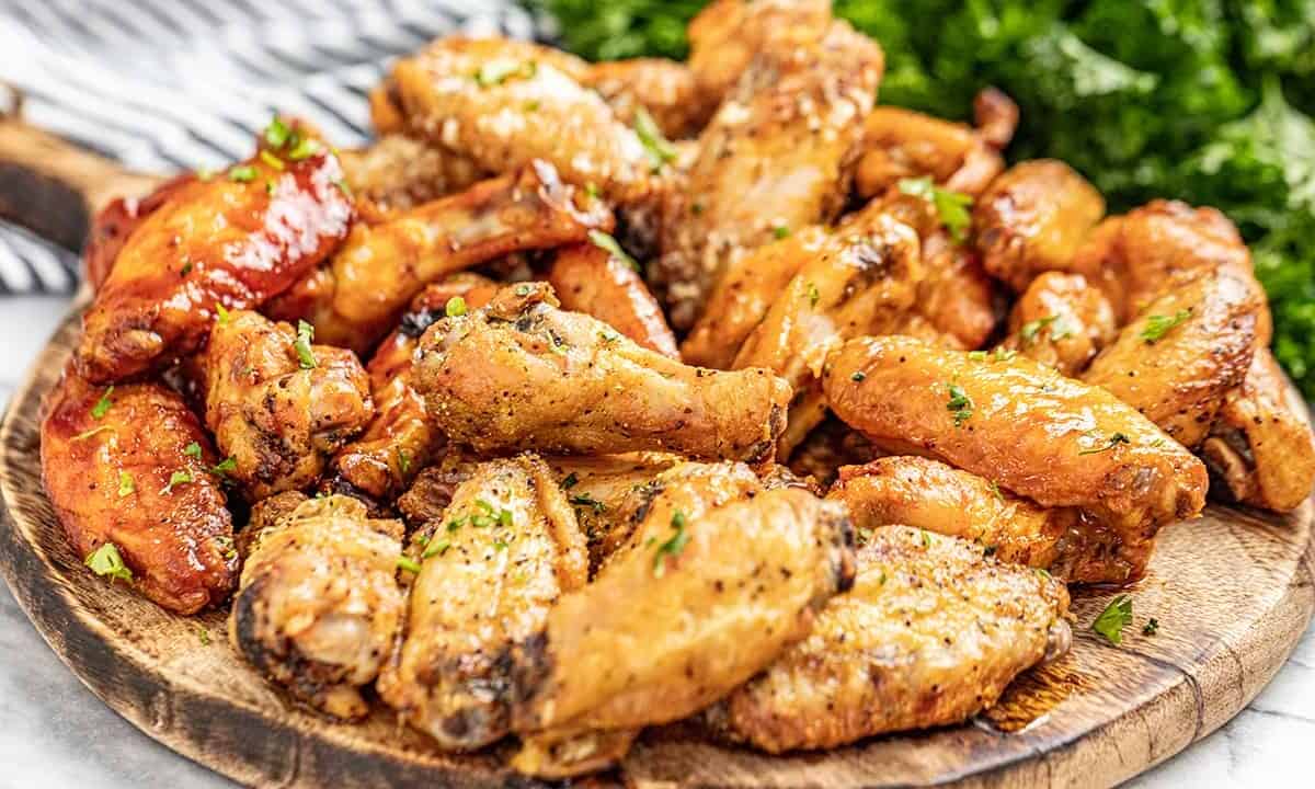 A wooden serving board filled with chicken wings, sprinkled in parsley