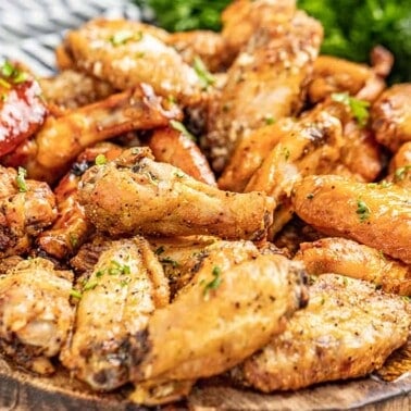 A wooden serving board filled with chicken wings, sprinkled in parsley