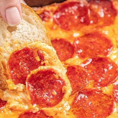 Hand dipping bread into pizza dip in a skillet