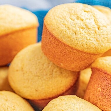 A basket lined with a towel and filled with cornbread muffins.