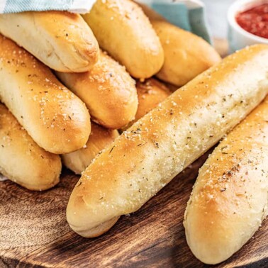 Breadsticks wrapped in a blue towel with marinara sauce in a bowl on the side.