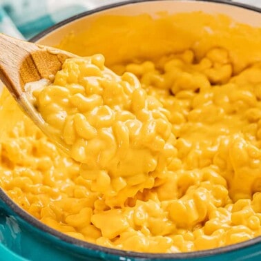 Close up view of Mac and cheese in a large pot with a wooden spoon.