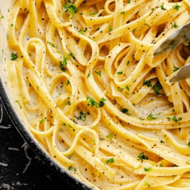 A close up overhead shot of a pot filled with fettuccine alfredo, with tongs set inside to serve.