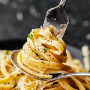 A close up view of a fork dishing up a serving of authentic fettucine alfredo.