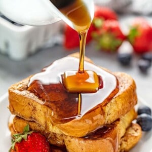 A stack of French Toast with a pad of butter on it all on a white plate with some berries on it.