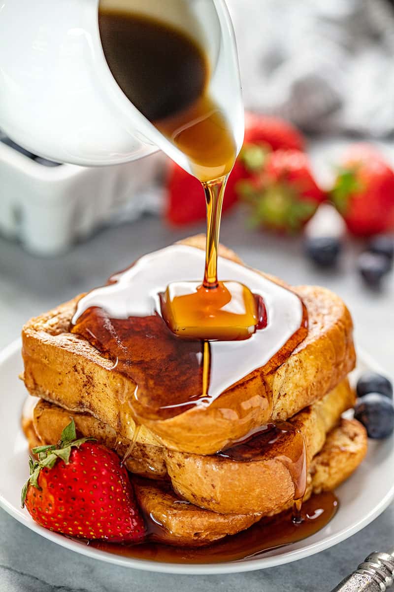 A stack of French Toast with a pad of butter on it all on a white plate with some berries on it.