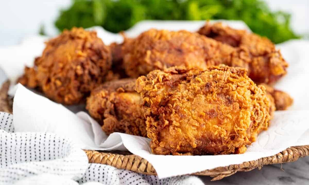 Angled view Crispy Fried Chicken on a paper towel on a wicker basket style platter.