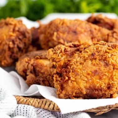 Angled view Crispy Fried Chicken on a paper towel on a wicker basket style platter.