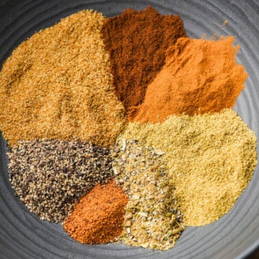 Overhead view, looking into a small black bowl with the individual spices needed to make Garam Masala separated from each other.