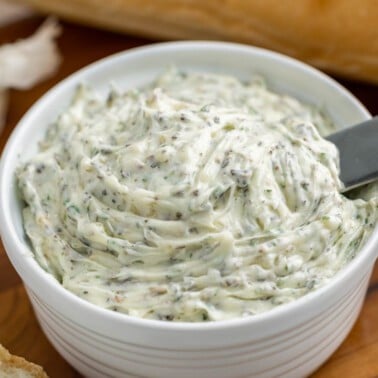 Close up view of homemade garlic butter in a small white dish with a spreading knife.