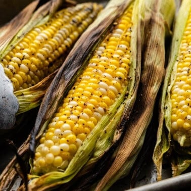 Grilled corn on the cob in their husks with a pair of tongs.