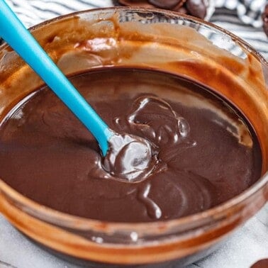 A bowl of chocolate ganache surrounded by chocolate cupcakes with ganache frosting.