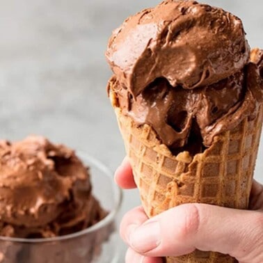 Close up of Chocolate Peanut Butter Banana healthy ice cream in a waffle cone with a few scoops in a clear dish in the background..