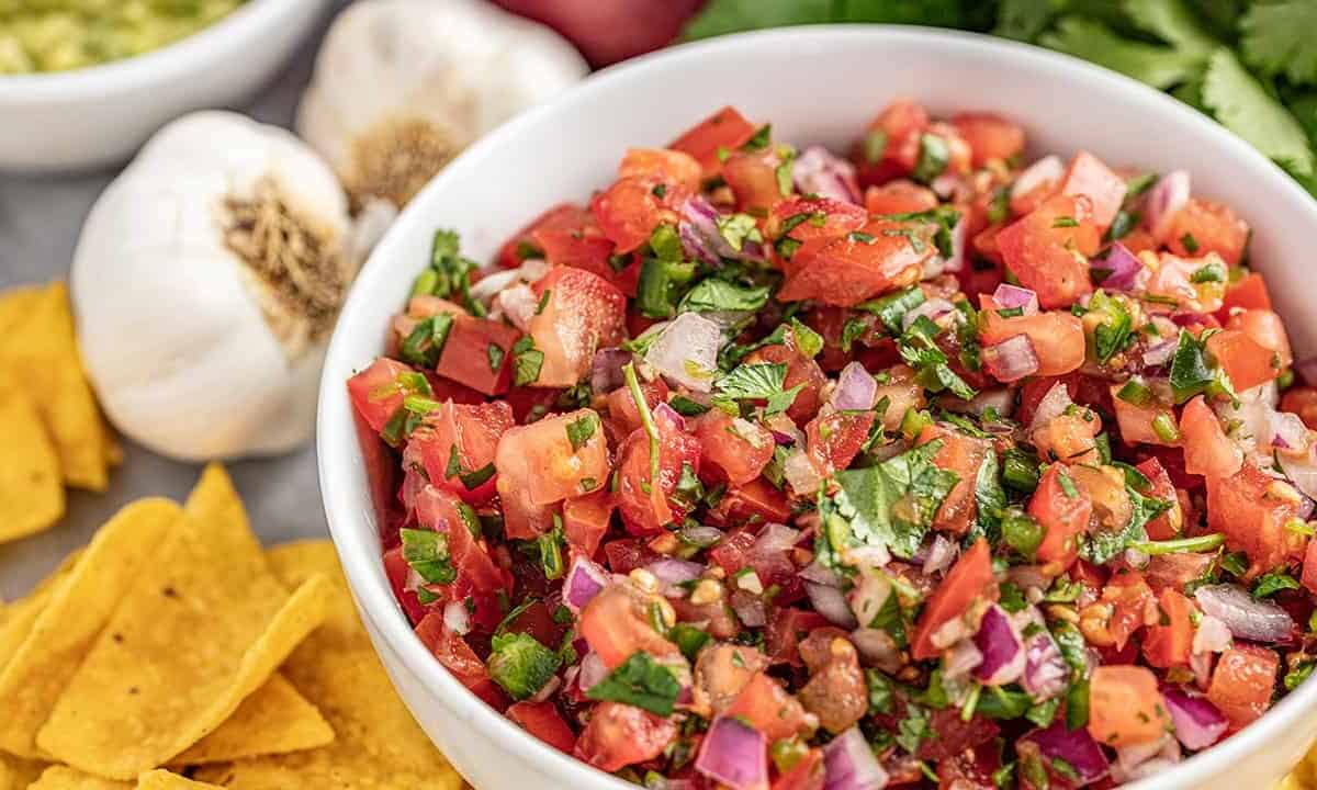 Homemade salsa in a bowl surrounded by chips and garlic