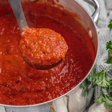 A ladle full of spaghetti sauce being removed from a large stockpot.