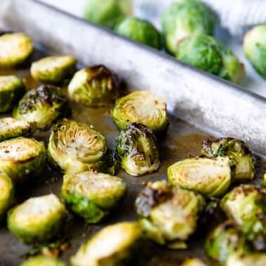 Roasted Brussel Sprouts on a baking sheet with raw sprouts in the background.