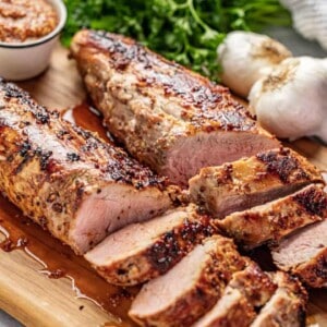 Angled view of a juicy and tender Honey Dijon Garlic Roasted Pork Tenderloin cut into slices on a wood cutting board.