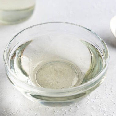 Looking into a small glass bowl filled with simple syrup with a spoon full of sugar next to it.